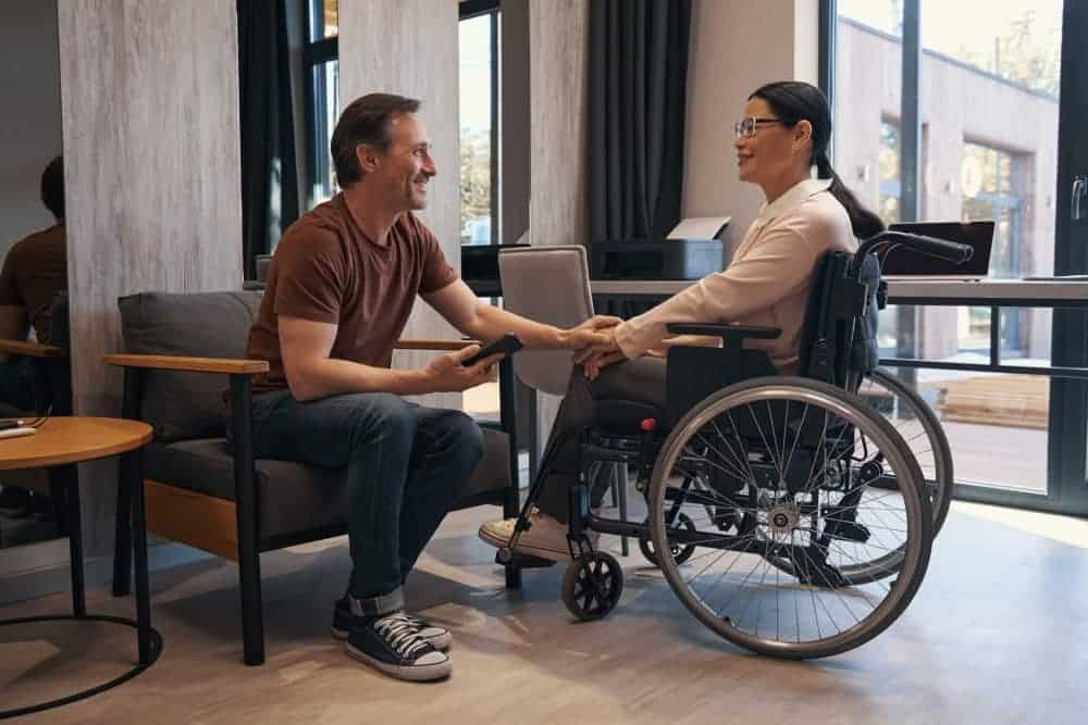 A man in a wheelchair is shaking hands with a woman in an office.
