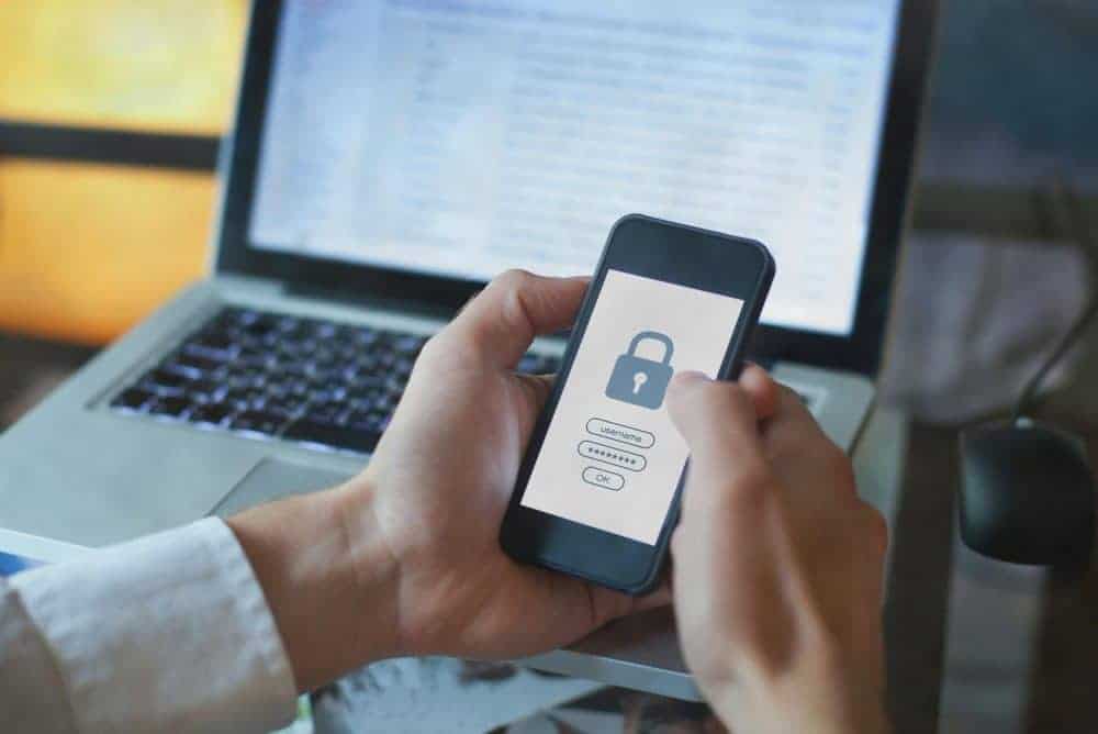 A person holding a phone with a padlock on it in front of a laptop.