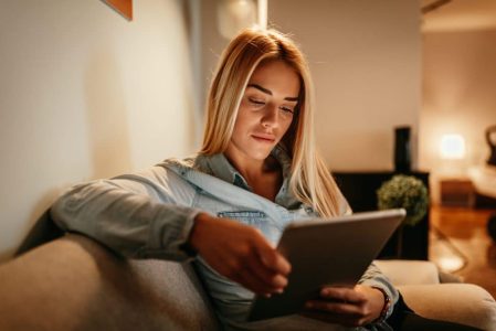 A woman sitting on a couch looking at a tablet computer.