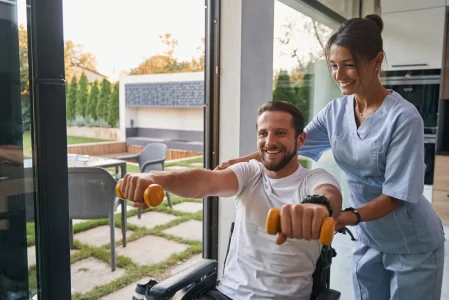 A nurse is helping a man in a wheelchair with dumbbells.